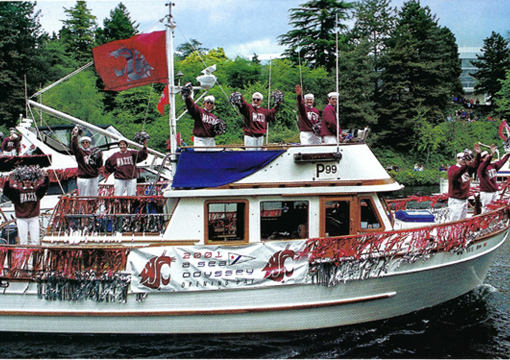 People in WSU gear on a boat wave at the camera.