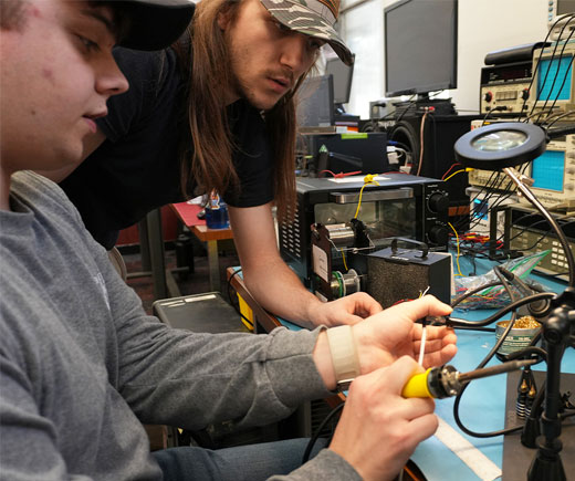 Two students sitting at tech bench.