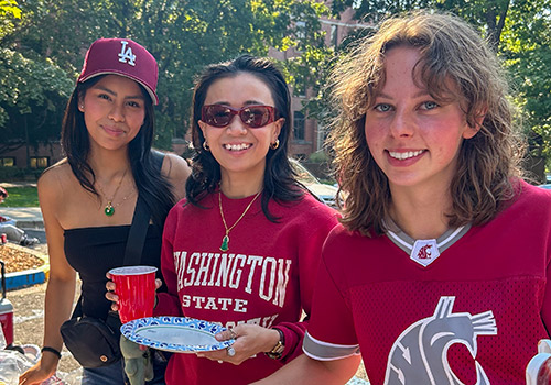 Three students at tailgate barbecue in WSU shirts smiling at camera.