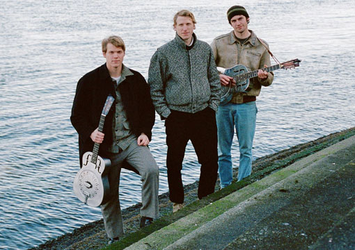 The 3 Brudi Brothers standing outside holding instruments.